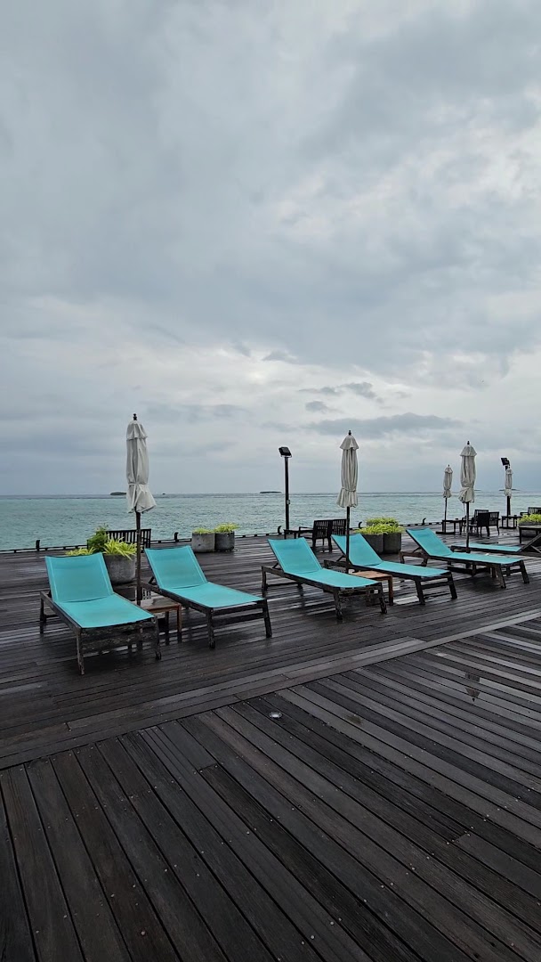 Koka terase ar tirkīza krāsas zviļņiem un saulessargiem Kuredu Island Resort & Spa kūrortā mākoņainā dienā