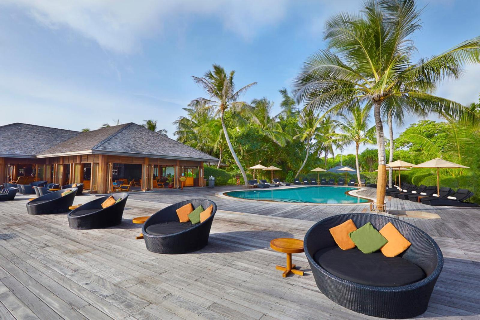 Kuredu Island Resort & Spa baseina terase ar stilīgiem dārza mēbelēm, saulessargiem un palmām Maldīvu salu kūrortā