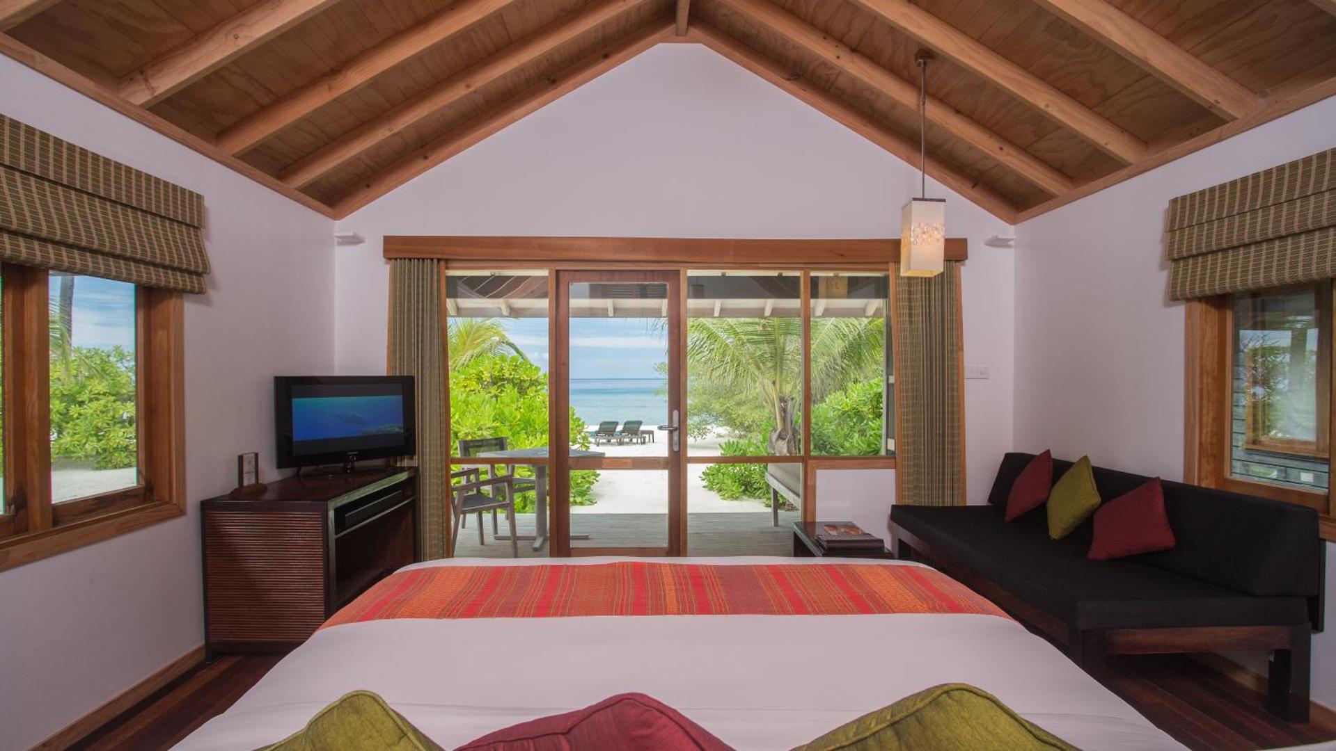 Kuredu Island Resort & Spa pludmales villas interjers ar skatu caur stikla durvīm uz balto smilšu pludmali un okeānu