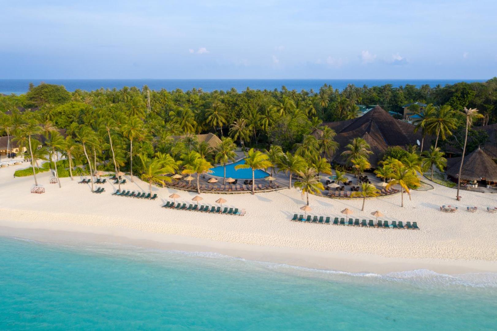Kuredu Island Resort & Spa pludmales zona ar saulessargiem, zviļņiem, āra baseinu un palmām pie tirkīza krasta