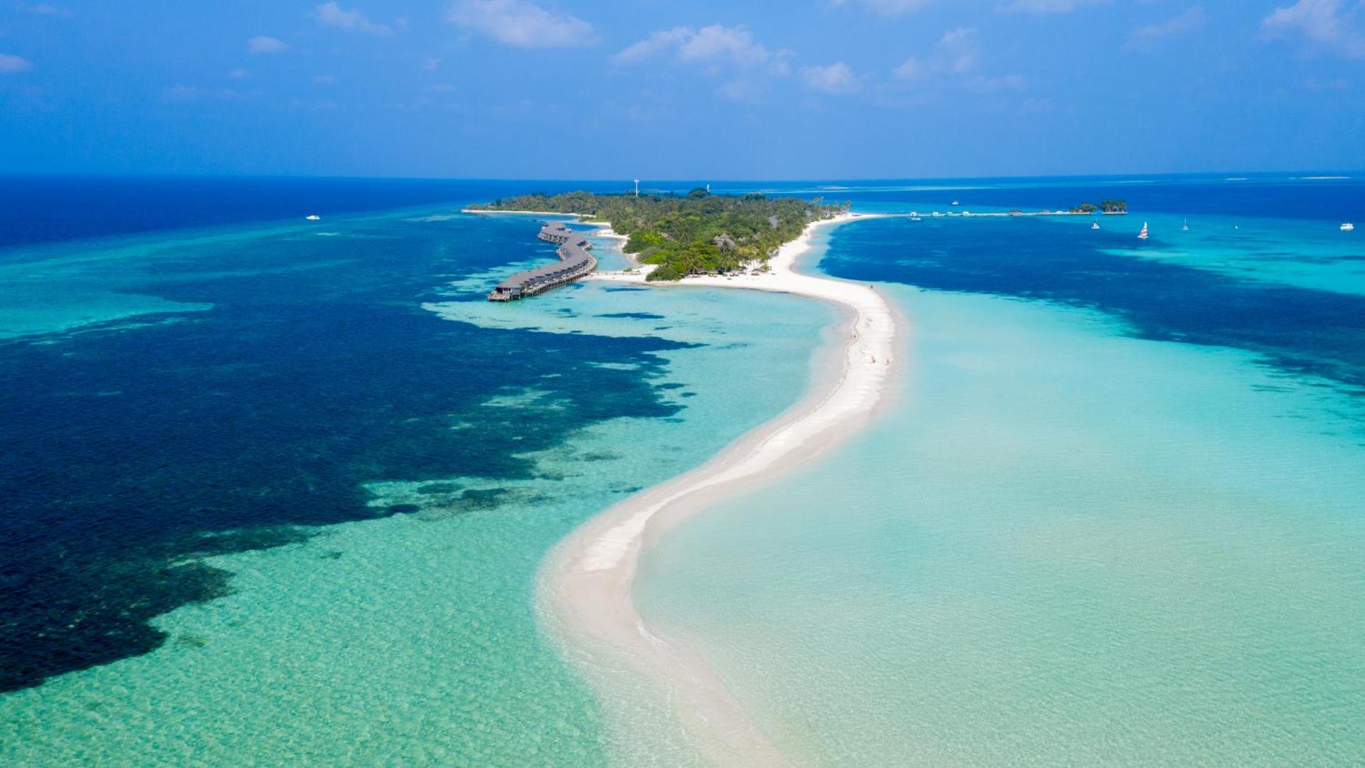 Kuredu Island Resort & Spa aerofoto uzņēmums ar garu smilšu strēli, tirkīza ūdeni un bungalo rindu Maldivu salās