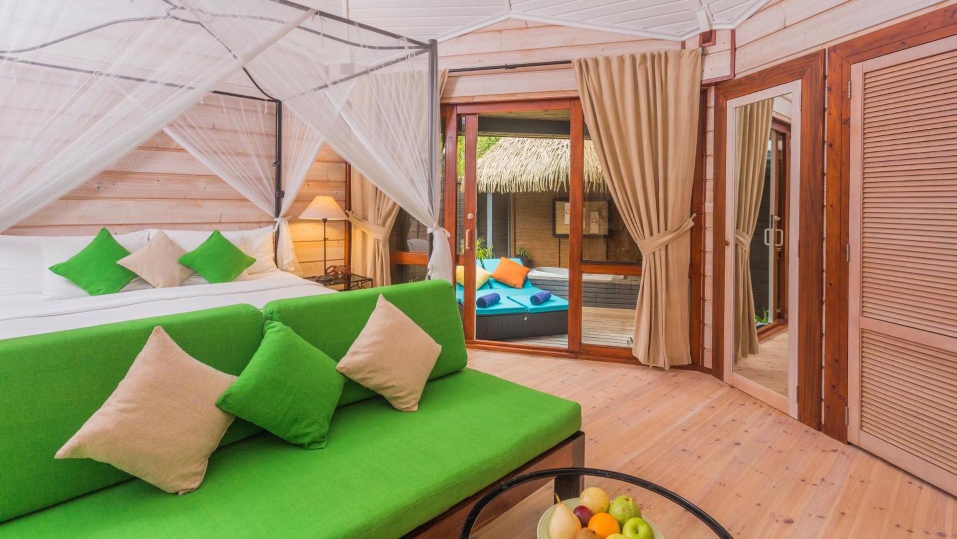 Kuredu Island Resort & Spa gaišs numurs ar koka apdari, zaļiem akcentiem, baldahīna gultu un skatu uz terasi ar džakuzi