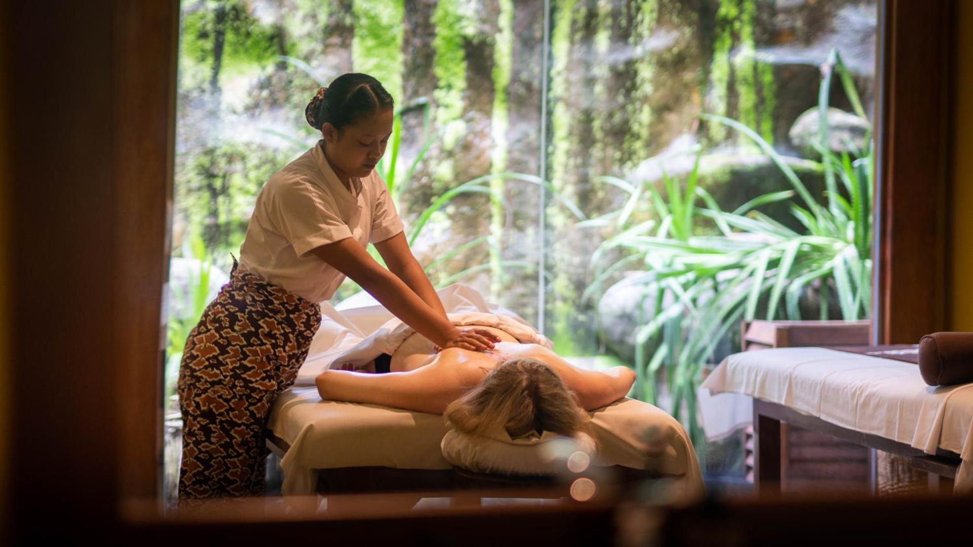 Adaaran Select Meedhupparu spa procedūra ar masāžu, ko veic profesionāla darbiniece mierīgā gaisotnē ar skatu uz tropu zaļumiem.