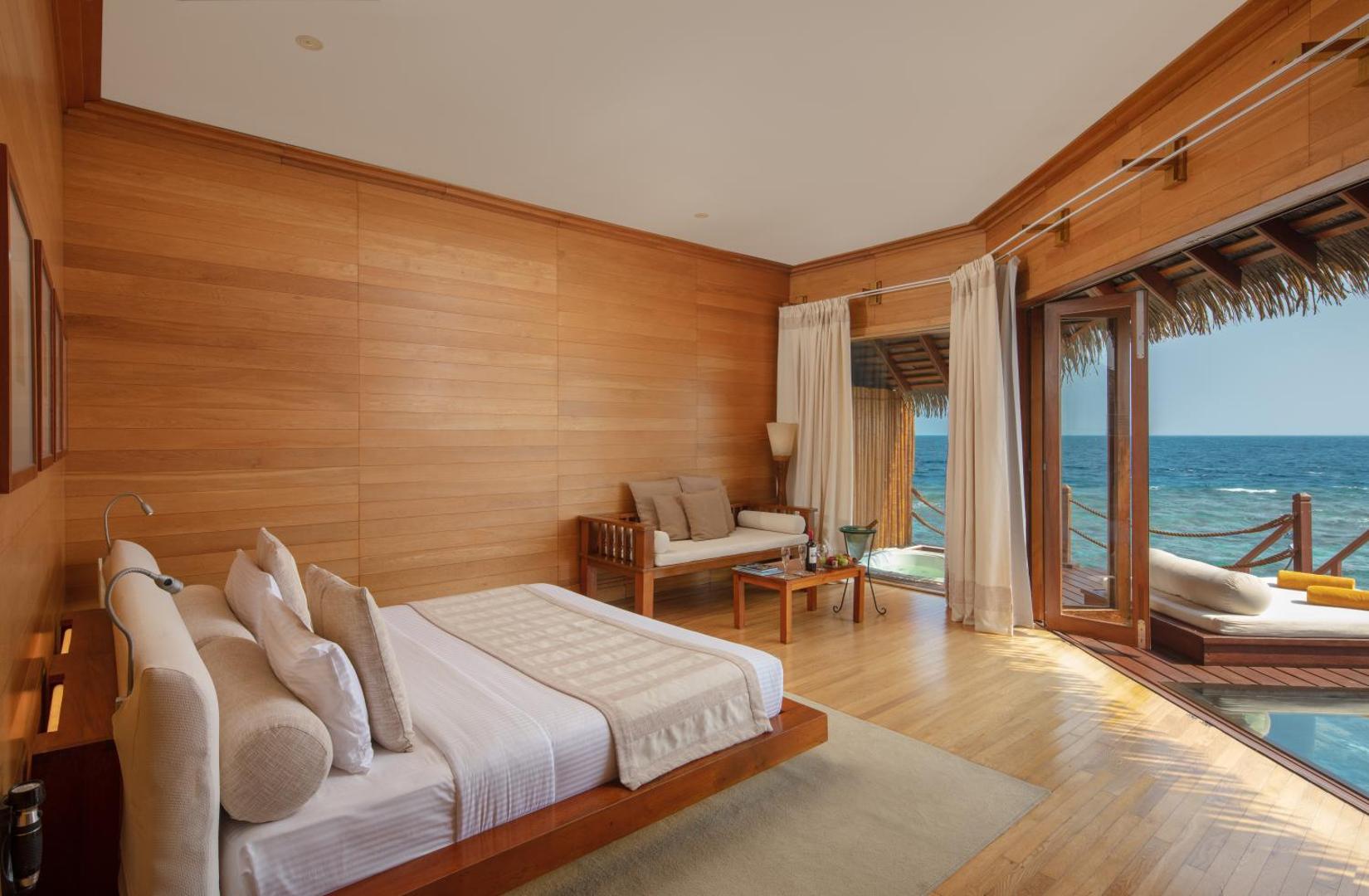 Adaaran Select Meedhupparu ūdens villas numurs ar koka apdari, plašu gultu un tiešu skatu uz okeānu Maldīvu salās.