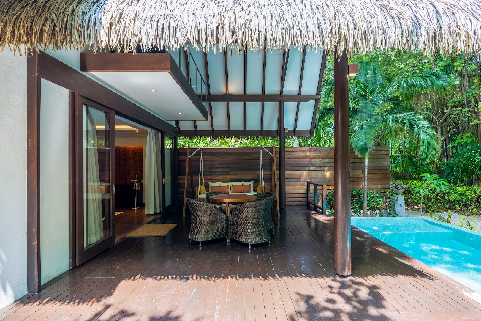 Adaaran Select Meedhupparu villas āra terase ar atpūtas mēbelēm, šūpuļkrēslu un privātu baseinu tropu zaļumu ielenkumā.