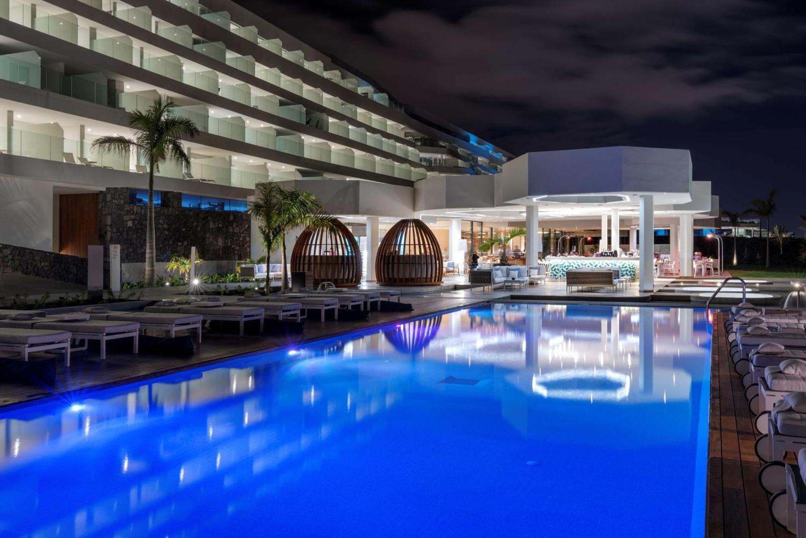 Royal Hideaway Corales Beach izgaismots āra baseins un viesnīcas fasāde nakts laikā ar bāra zonu Tenerifē