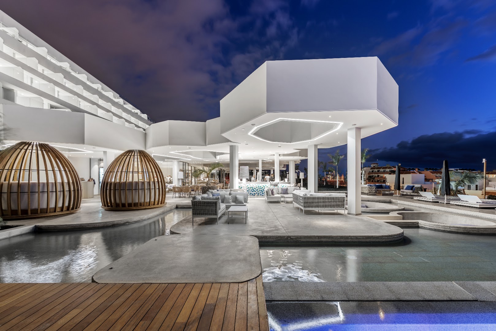 Royal Hideaway Corales Beach atpūtas zona ar baseiniem un stilīgām atpūtas ložām vakarā — bārs un dīvāni pie ūdens