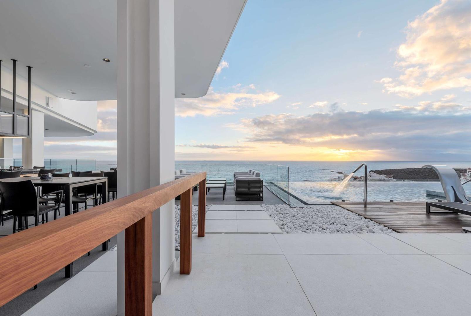 Royal Hideaway Corales Beach baseins ar pārplūdes malu un skatu uz okeānu — moderna terase ar atpūtas zonu saulrietā