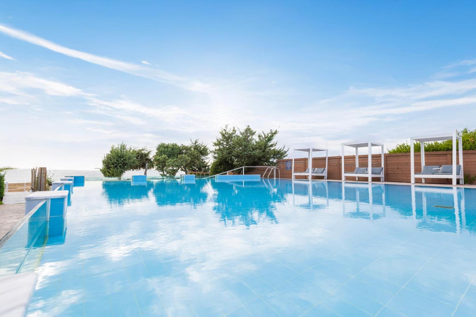 Sandy Beach Resort āra baseins ar pārplūdes malu un saulessargiem piekrastē, skats uz jūru un debesīm