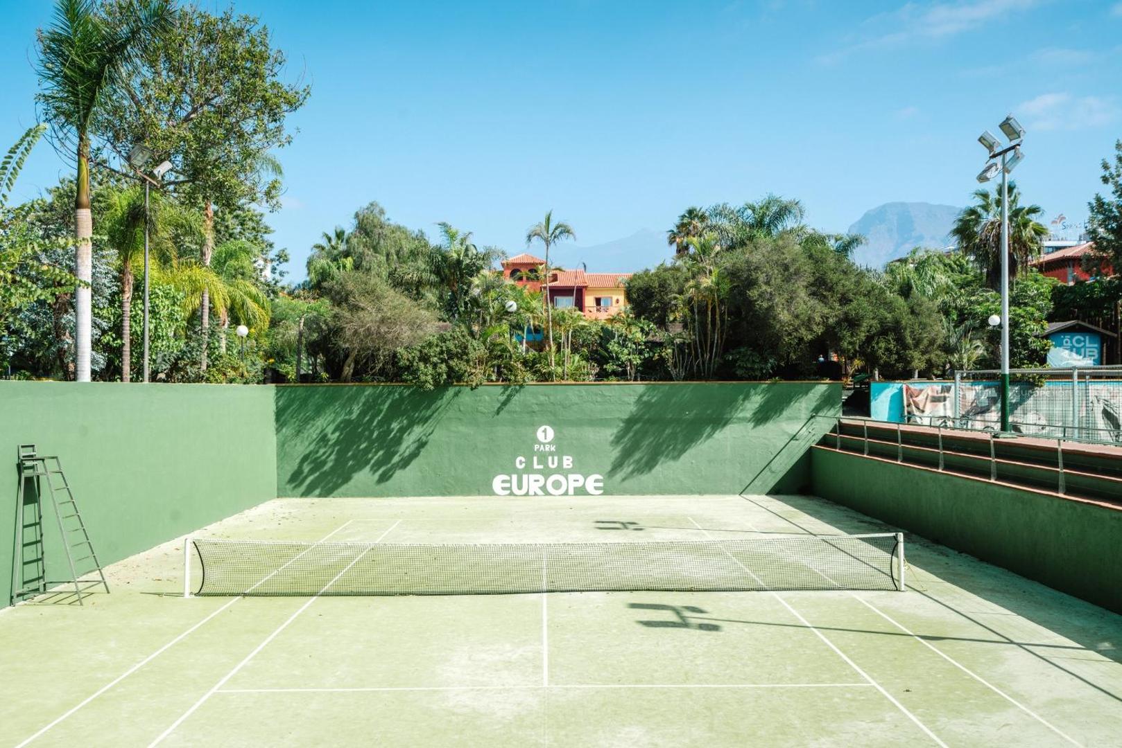 Park Club Europe tenisa korts ar zaļu segumu un apkārtējo apstādījumu skatu Tenerifē, piemērots viesu sporta aktivitātēm
