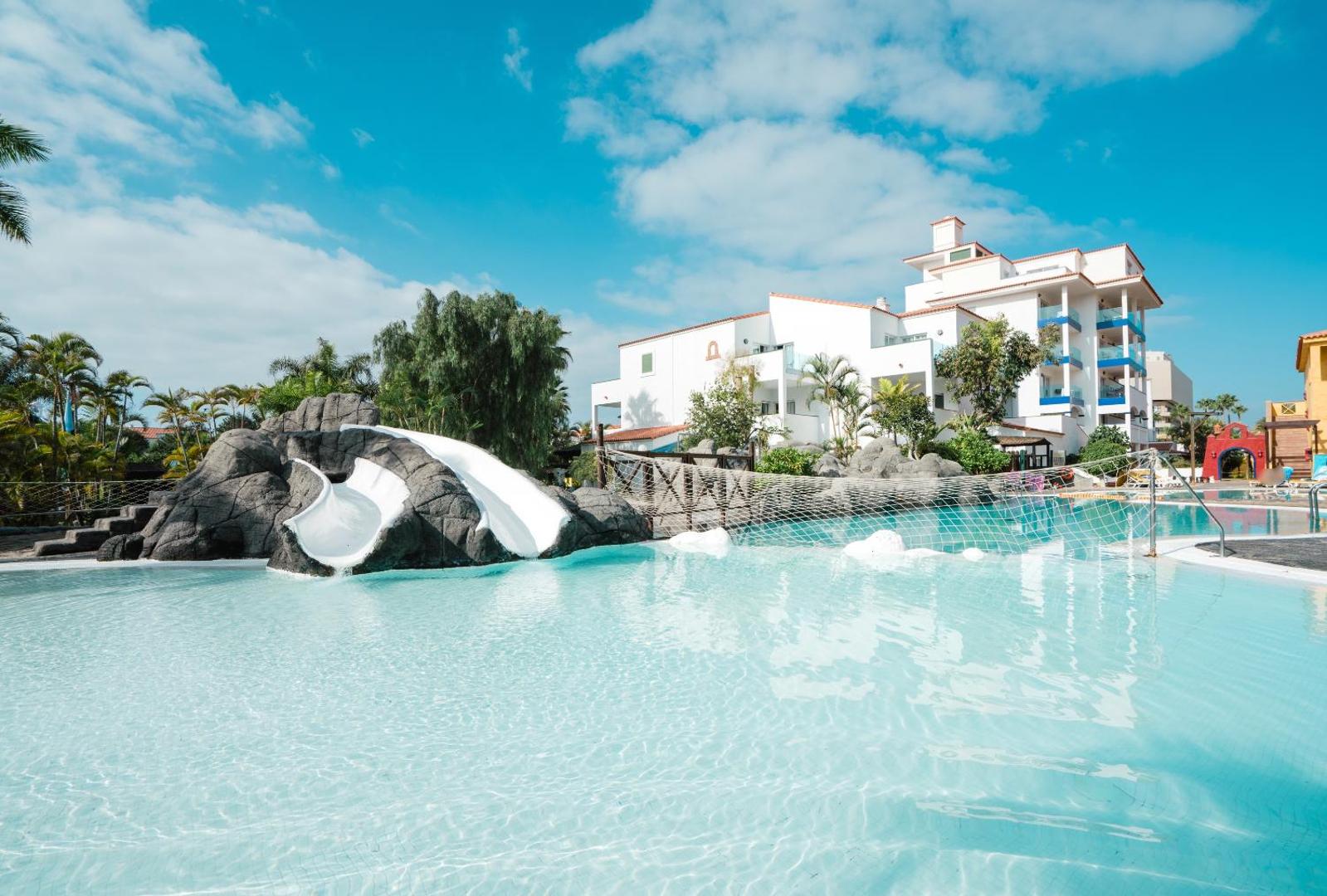 Park Club Europe viesnīcas bērnu baseins ar ūdens slidkalniņu Tenerifē — gaišs ūdens, mākslīgo klinšu elementi un viesnīcas korpusi fonā