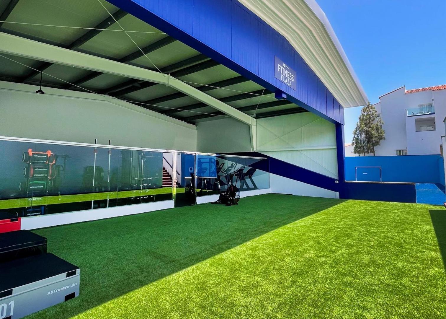 Park Club Europe āra fitness zona Fitness Plaza ar mākslīgo zālienu un trenažieriem zem nojumes Tenerifes saulē.