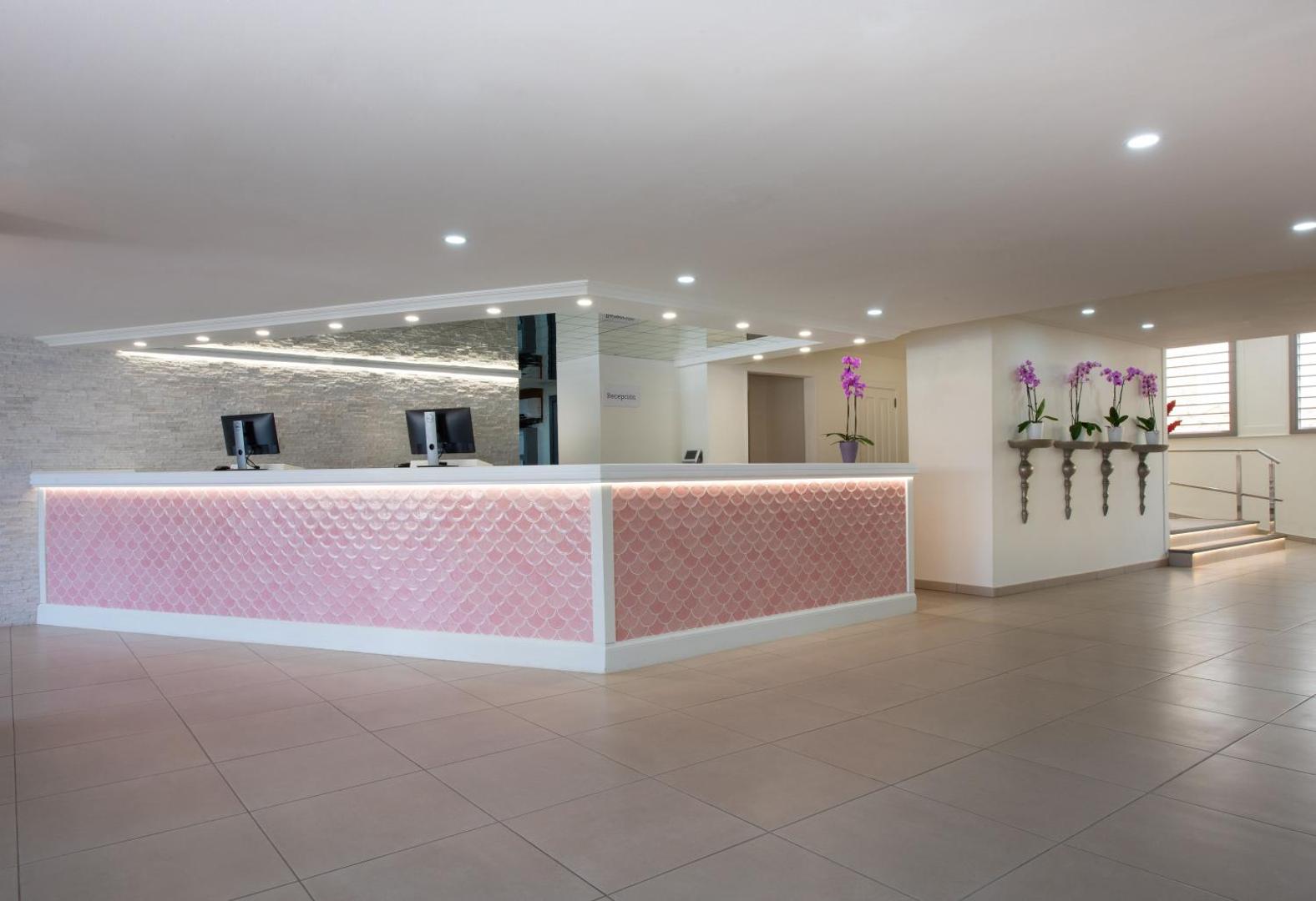 Ole Tropical Tenerife viesnīcas recepcijas zona ar rozā dekoratīvu paneli, baltu leti un orhideju ziediem