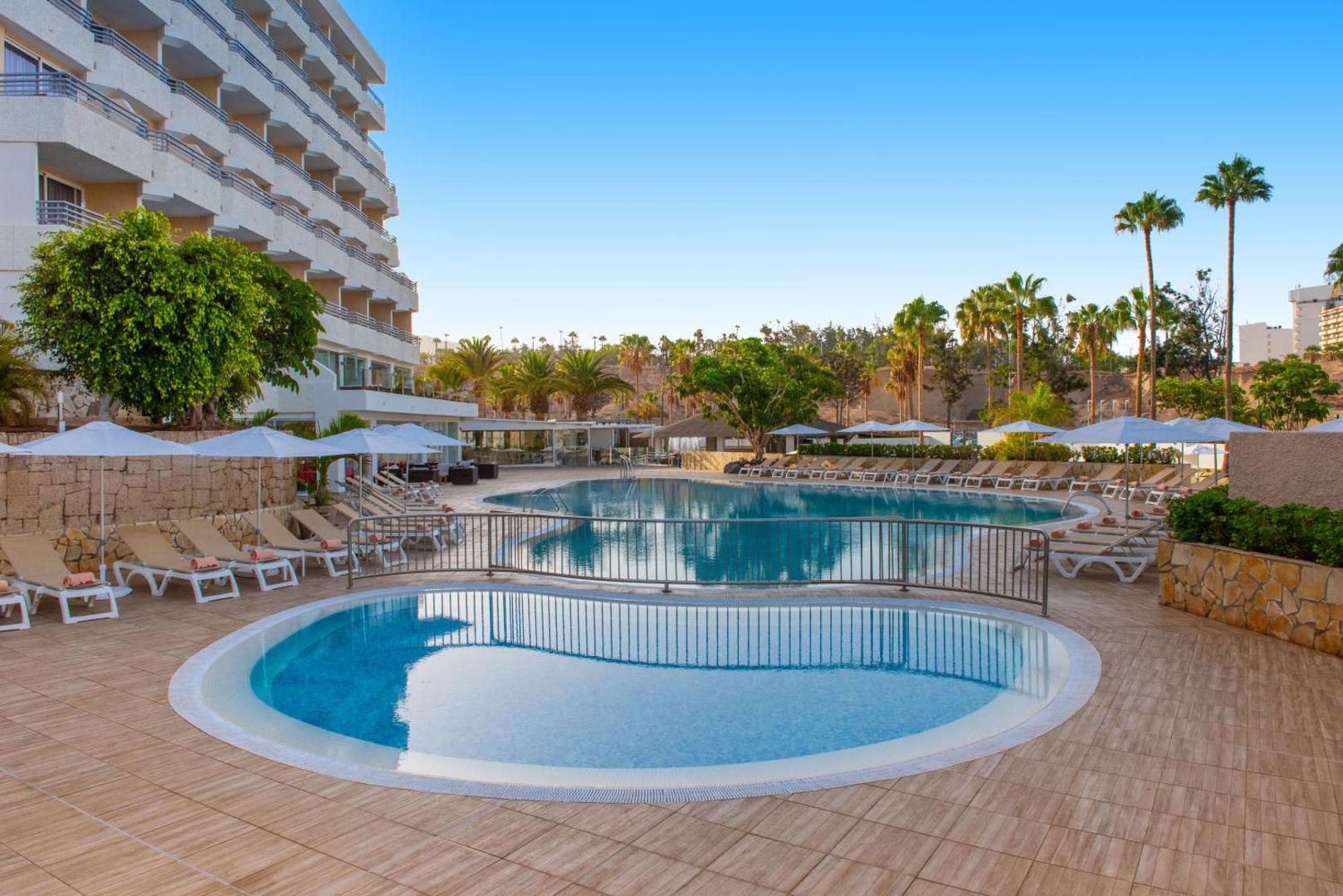 Viesnīcas Ole Tropical Tenerife āra baseinu zona ar bērnu baseinu priekšplānā un galveno ēku fonā Tenerifes dienvidos
