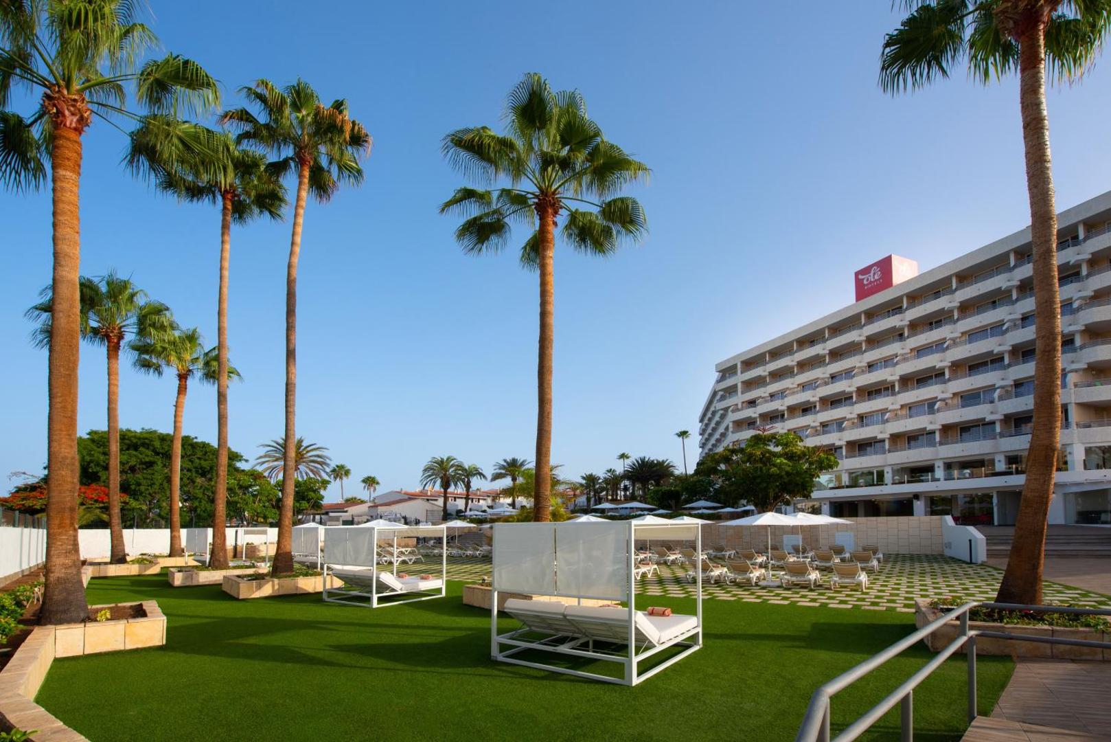 Ole Tropical Tenerife viesnīcas atpūtas zona ar zālāju, palmām un moderniem sauļošanās krēsliem Tenerifes dienvidos, netālu no pludmales