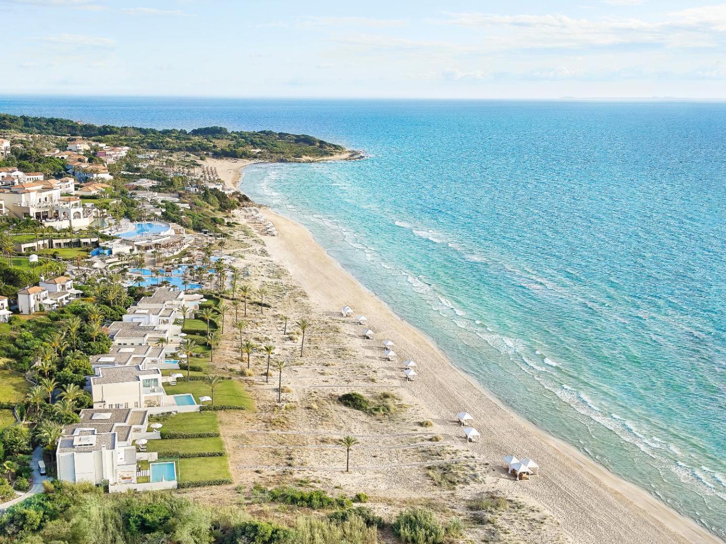 Grecotel Mandola Rosa kūrorta panorāmas skats no putna lidojuma uz balto smilšu pludmali, villām un zilajiem baseiniem Peloponēsā.