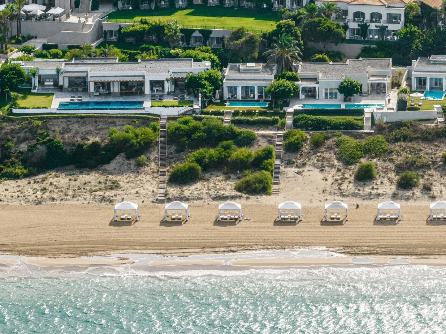 Grecotel Mandola Rosa luksusa villas ar privātiem baseiniem piekrastes kāpās un baltām teltīm privātajā pludmalē.