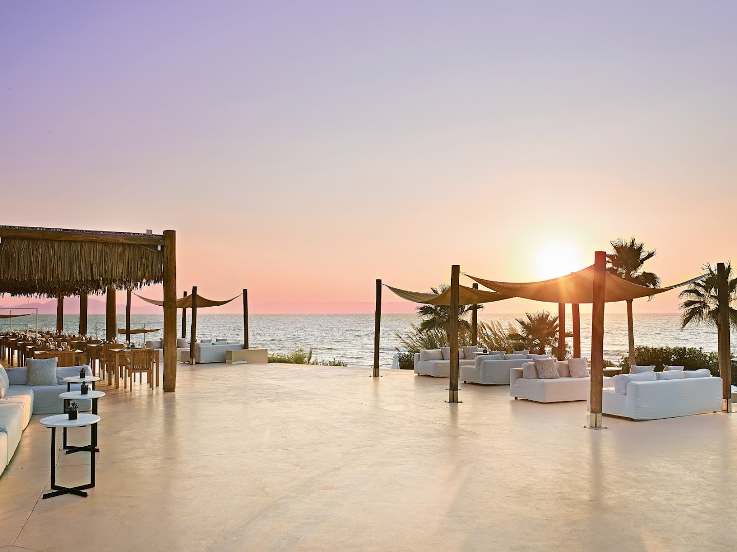 Grecotel La Riviera āra terase saulrieta laikā ar skatu uz Jonijas jūru, mīkstajiem dīvāniem un restorāna zonu Peloponēsā.