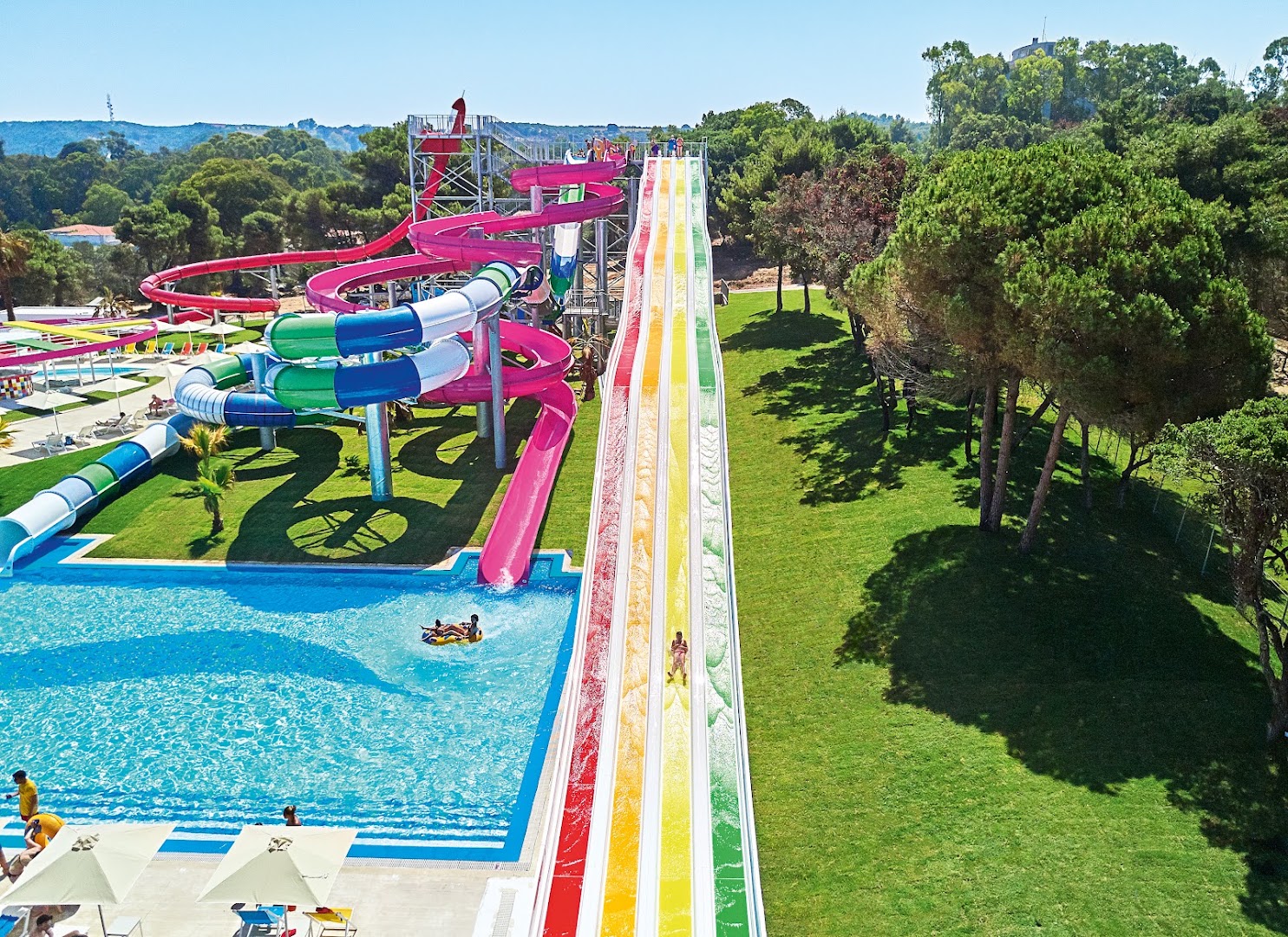 Grecotel La Riviera viesnīcas akvaparks Peloponēsā ar krāsainiem ūdens slidkalniņiem, lielu baseinu un zaļu dārza zonu saulainā dienā