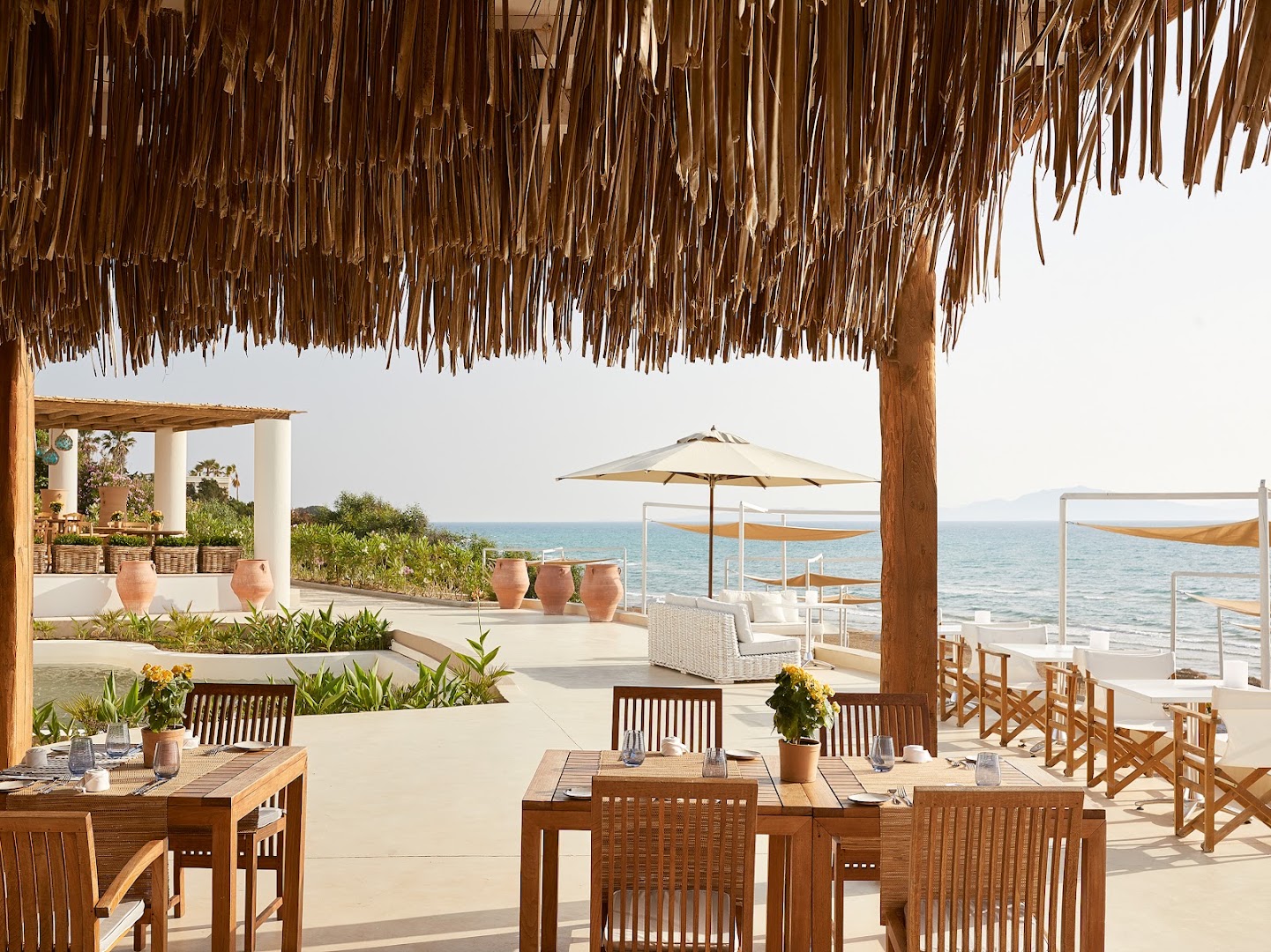 Grecotel La Riviera āra restorāna terase ar koka galdiem un skatu uz jūru Peloponēsā — Vidusjūras stila dizains zem nojumes