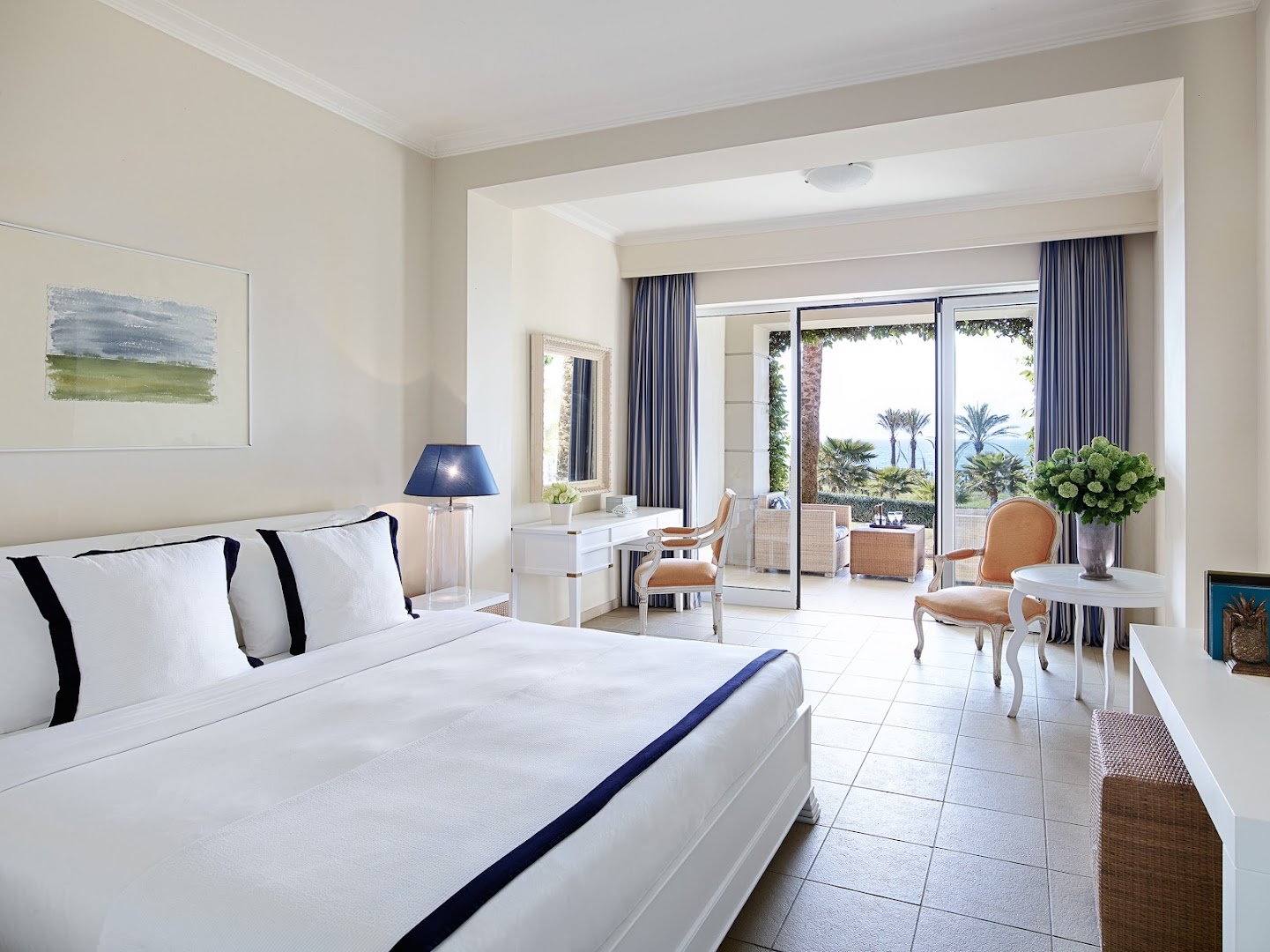 Grecotel La Riviera gaišs viesnīcas numurs ar balkonu, no kura paveras skats uz dārzu un jūru Peloponēsā