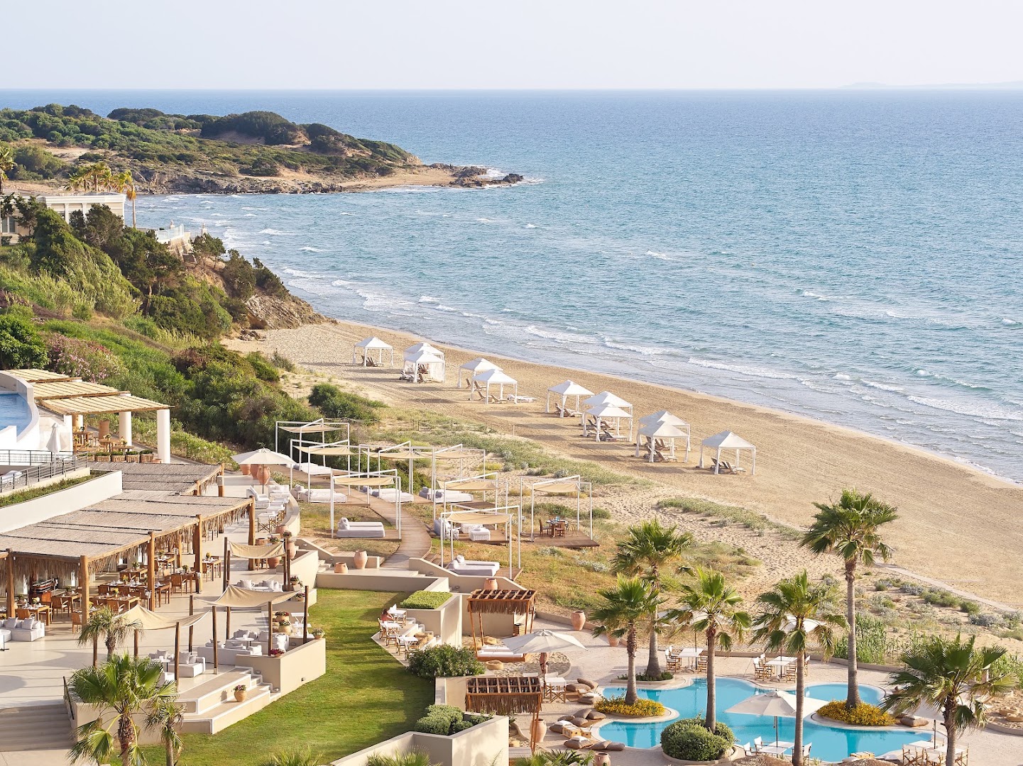 Grecotel La Riviera privātā smilšu pludmale ar saulessargiem un kūrorta terasēm Peloponēsas piekrastē — skats no augšas uz jūru