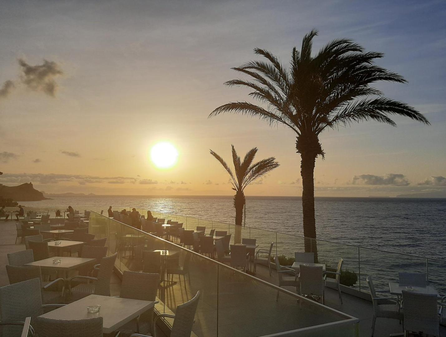 Rocamar Lido Resort āra terase saulrieta laikā Funšalā, Madeirā — skats uz okeānu, galdiņi un palmas vakara gaismā