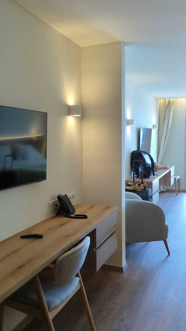Moderns Rocamar Lido Resort numura darba stūris ar koka galdu, krēslu un sienas apgaismojumu gaišos toņos