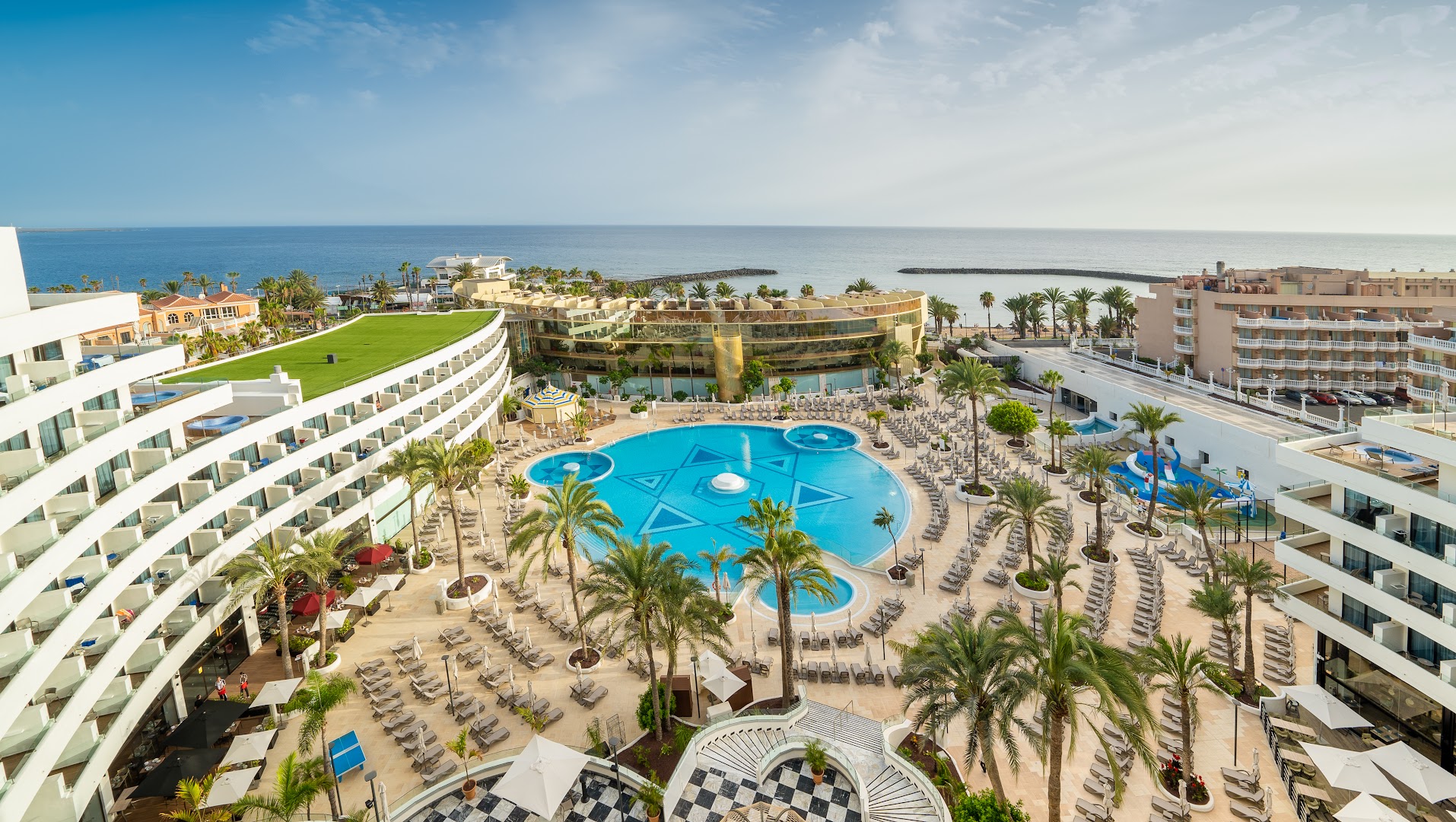 Panorāmas skats uz Mediterranean Palace plašo baseinu zonu, sauļošanās krēsliem un okeāna piekrasti Tenerifes dienvidos