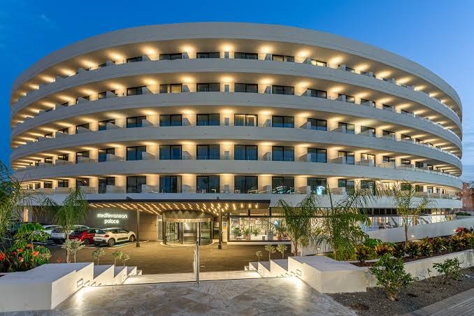 Viesnīcas Mediterranean Palace galvenā ēka un piebraucamais ceļš krēslas stundā ar dekoratīviem augiem un siltu apgaismojumu