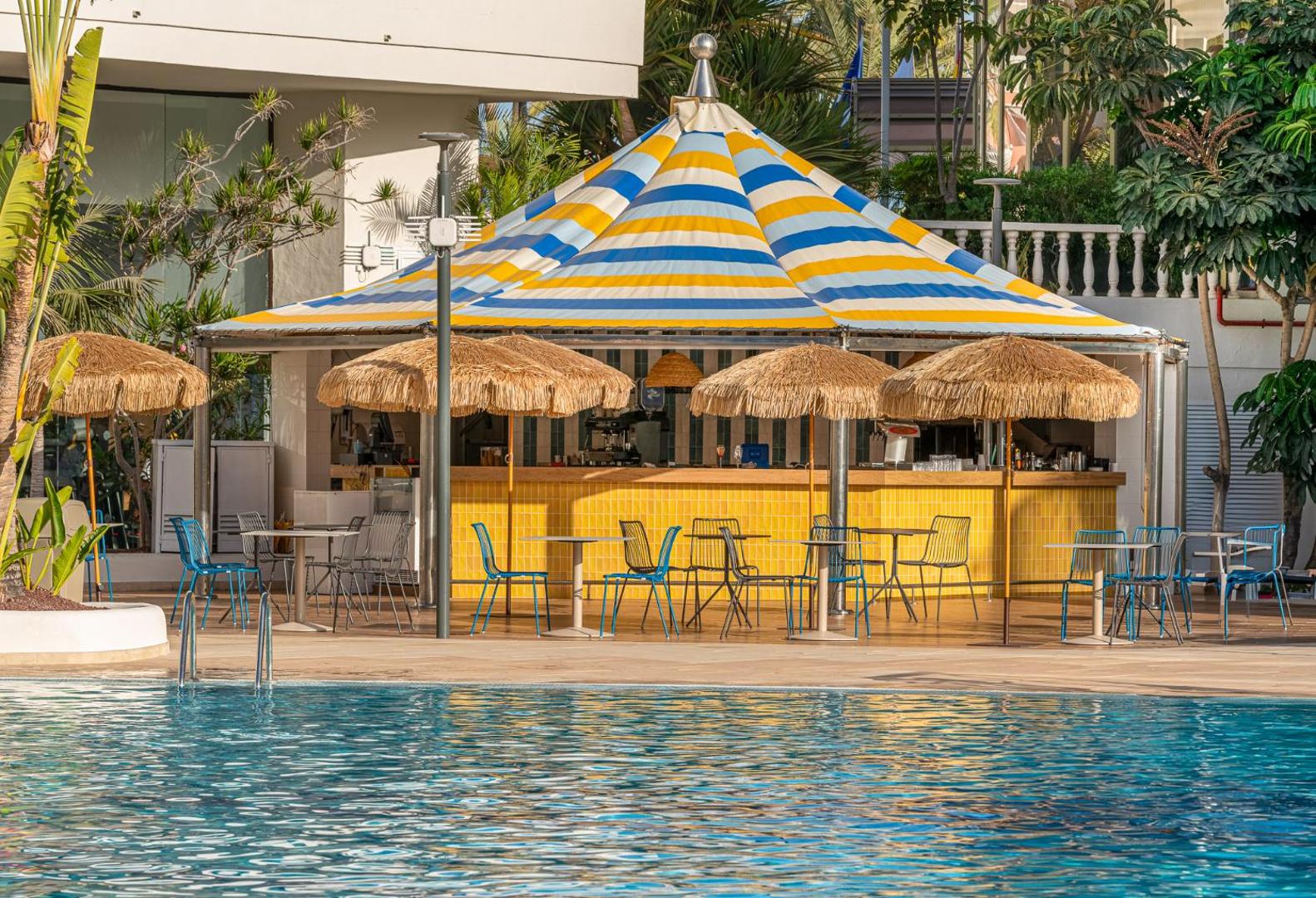 Tuvplāns Mediterranean Palace baseina bāram ar stilīgu svītrainu jumtu un pītiem saulessargiem Tenerifes kūrortā.
