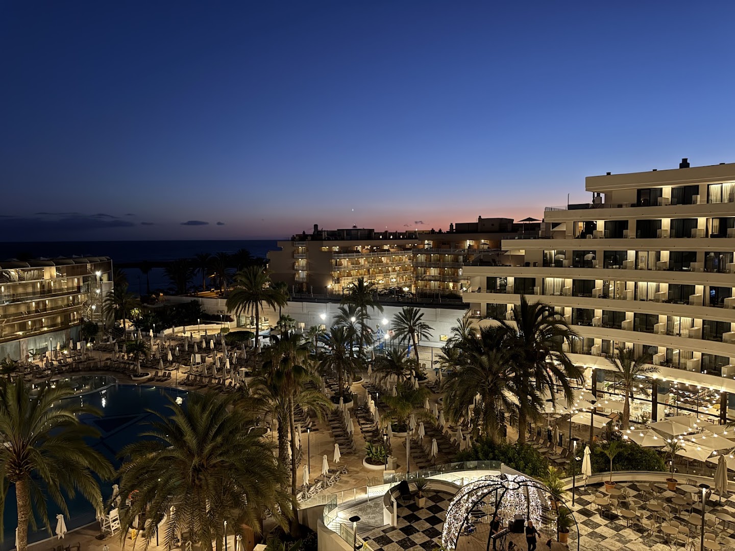 Viesnīcas Mediterranean Palace skats vakarā uz baseinu, palmām un apgaismoto fasādi Tenerifē, Kanāriju salās pie okeāna piekrastes