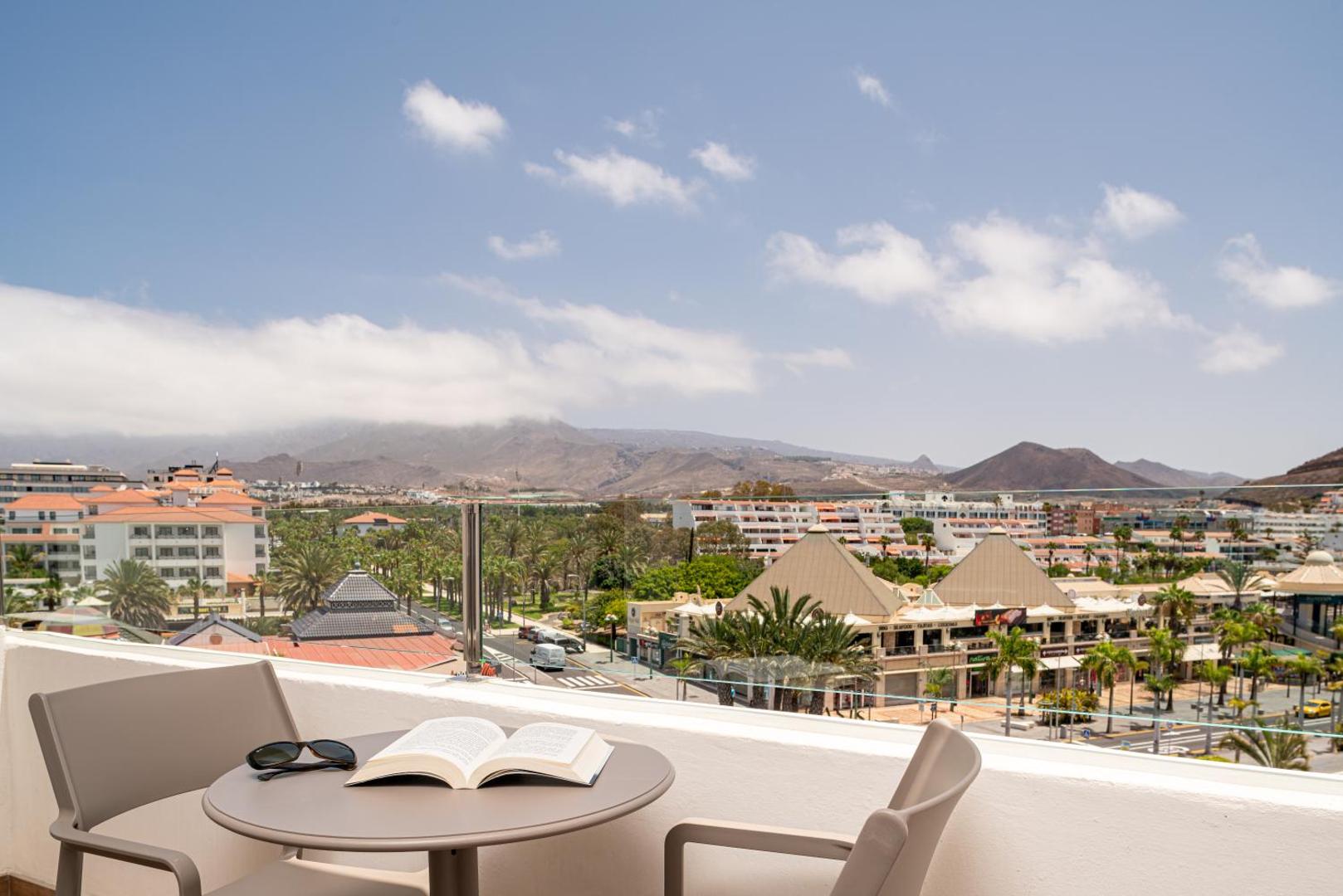 Skats no Mediterranean Palace terases uz Tenerifes kalniem un pilsētas panorāmu — atpūtas zona ar galdiņu un krēsliem