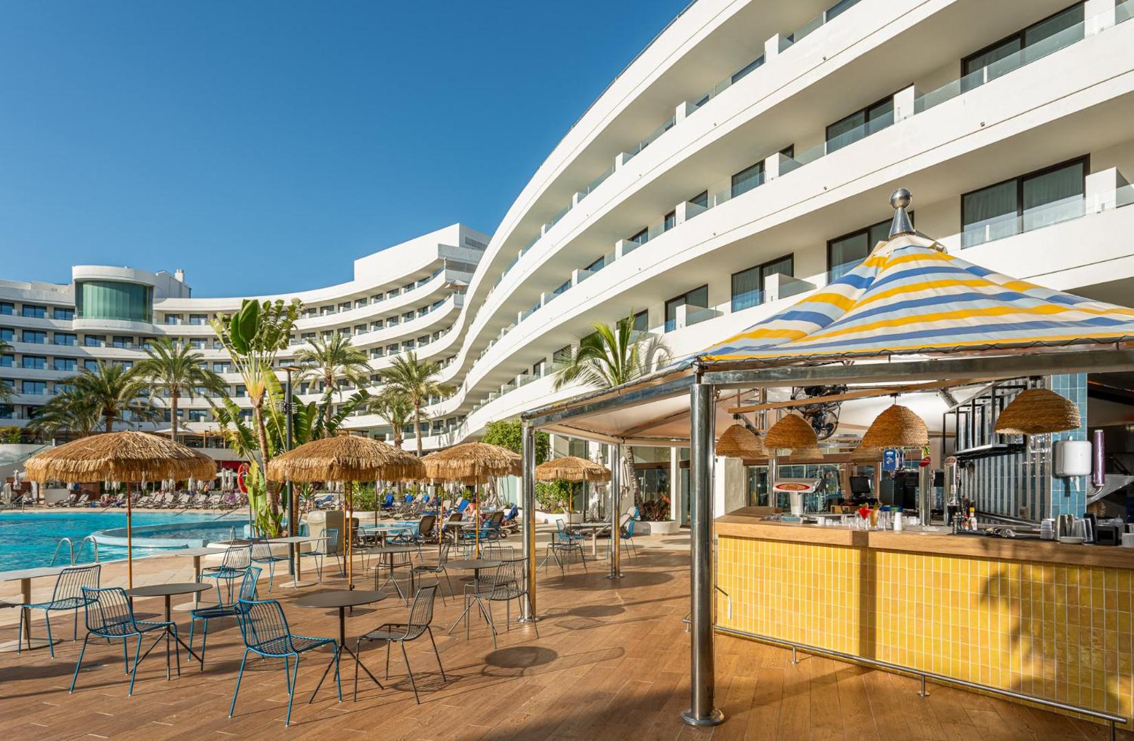 Mediterranean Palace baseina bārs ar dzeltenu apdari un saulessargiem dienas laikā Tenerifē — blakus galdiņi un krēsli atpūtai.