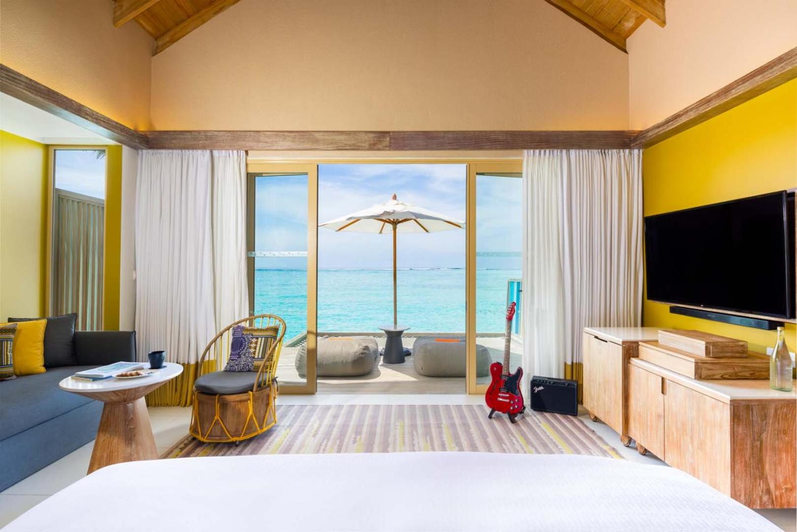 Hard Rock Hotel Maldives numurs ar izeju uz terasi, kur atrodas sēžammaisi, saulessargs un elektriskā ģitāra pie TV zonas.