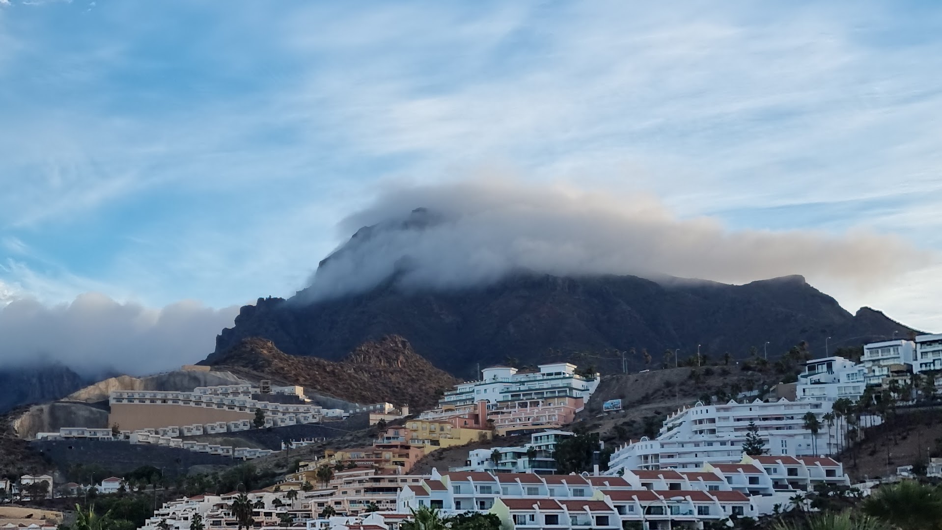 Malibu Park Apartments skats uz kalniem un apkārtējo apbūvi Tenerifē — mākoņos tīta kalna virsotne virs pilsētas kvartāliem