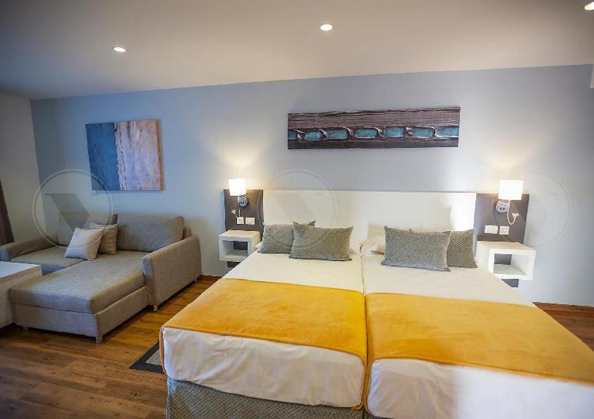 Malibu Park Apartments numura interjers ar divām gultām un pelēku stūra dīvānu Tenerifē — moderns apgaismojums un koka detaļas
