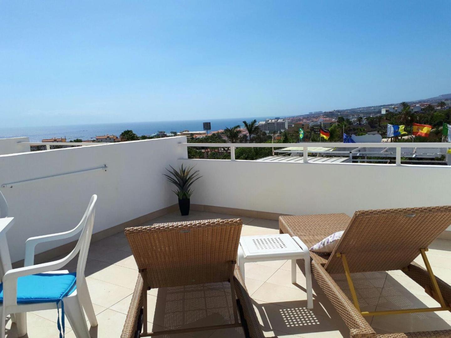Malibu Park Apartments saulaina jumta terase ar sauļošanās krēsliem un skatu uz okeānu Tenerifē — balta marga un zilas debesis
