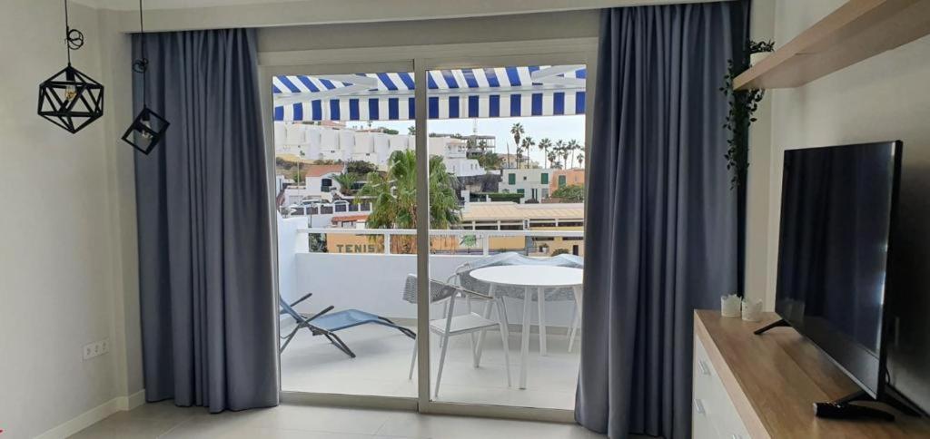 Malibu Park Apartments gaišs numurs ar balkonu un skatu uz pilsētu Tenerifē — interjerā zili aizkari, televizors un atpūtas zona