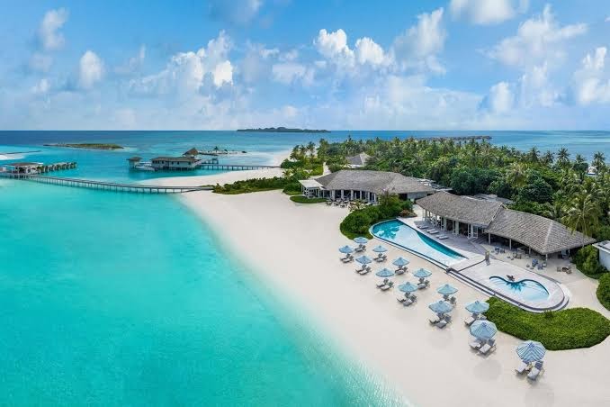 Le Meridien Maldives Resort & Spa galvenā pludmales zona ar atpūtas krēsliem, saulessargiem un koplietošanas baseinu pie okeāna krasta