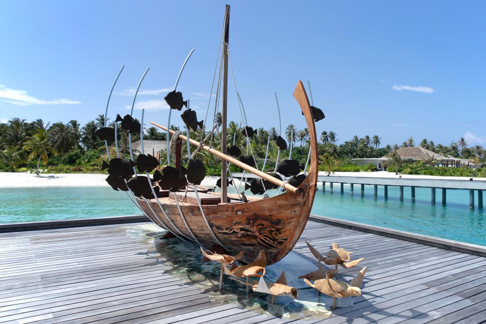 Le Meridien Maldives Resort & Spa koka laivas skulptūra uz koka klāja pie tirkīzzila ūdens Maldivu salās