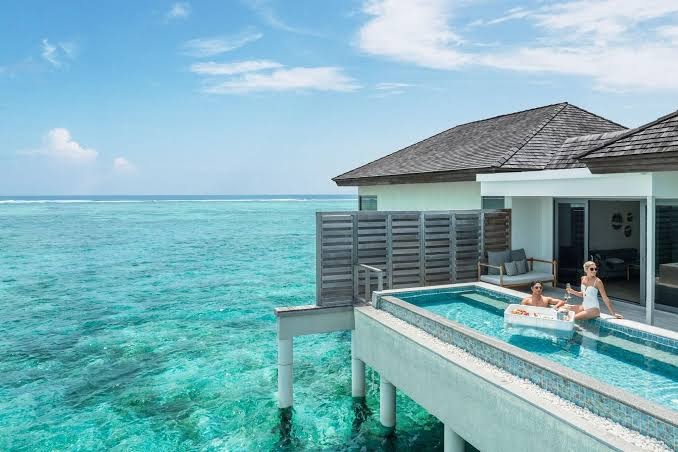 Le Meridien Maldives Resort & Spa ūdens bungalo terase ar privātu baseinu, kur pāris bauda brokastis ūdenī virs okeāna.
