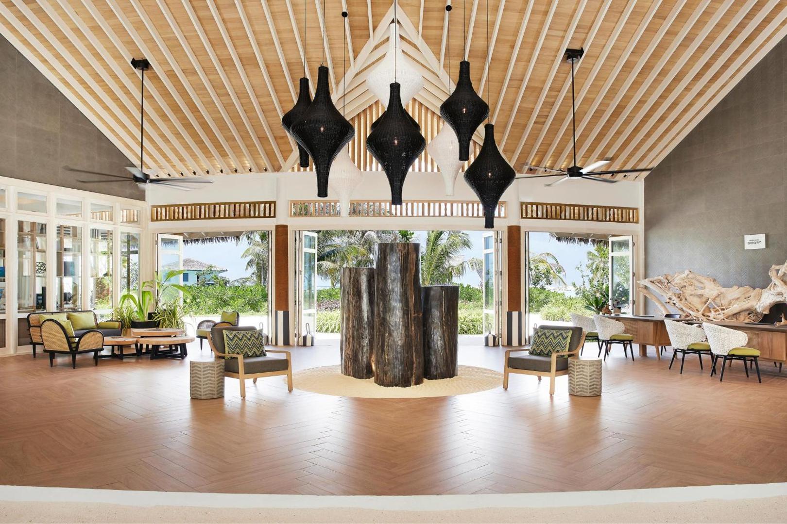 Le Meridien Maldives Resort & Spa viesnīcas lobby ar unikāliem dizaina gaismekļiem, koka apdari un atvērtu skatu uz dārzu