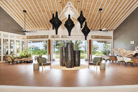 Le Meridien Maldives Resort & Spa atvērtā tipa reģistratūra ar skatu uz tropu zaļumiem un stilīgām atpūtas mēbelēm