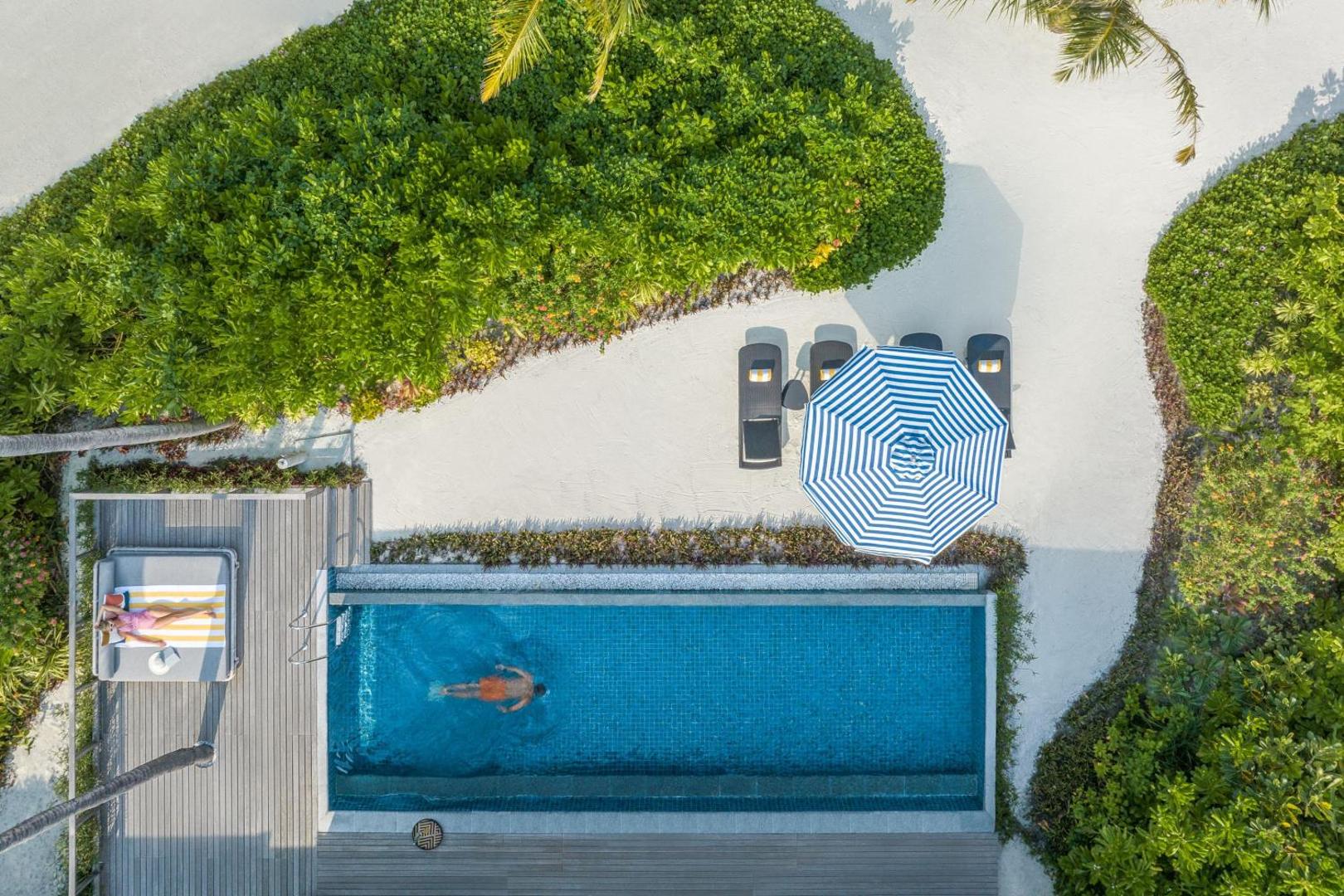 Le Meridien Maldives Resort & Spa privātais baseins pie villas, skats no augšas uz peldētāju, sauļošanās krēsliem un tropu zaļumiem.