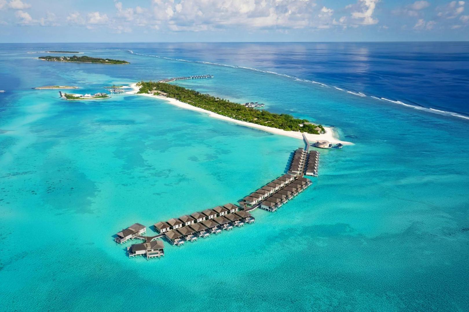 Le Meridien Maldives Resort & Spa kopskats no augšas — kūrorta sala ar ūdens villu laipām un koraļļu rifu Indijas okeānā