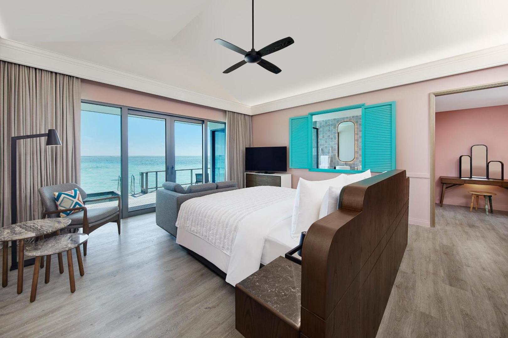 Le Meridien Maldives Resort & Spa gaišs numurs virs ūdens ar skatu uz okeānu, modernām mēbelēm un lieliem panorāmas logiem