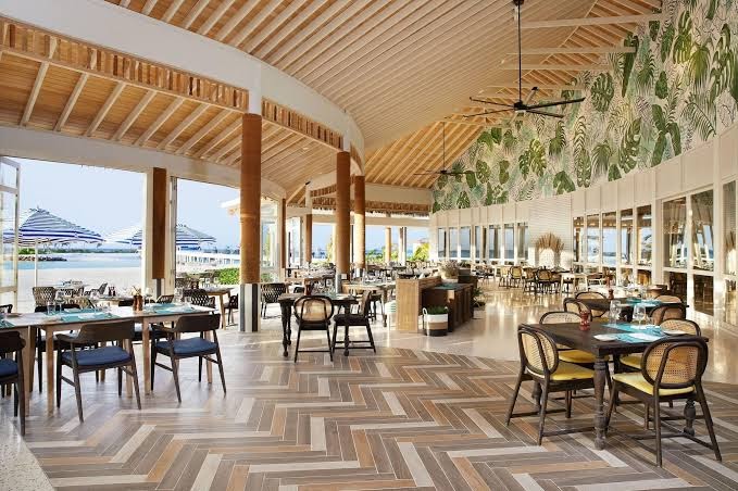 Le Meridien Maldives Resort & Spa plašais restorāns ar augstiem griestiem, tropu rakstiem un skatu uz okeānu Maldivu salās