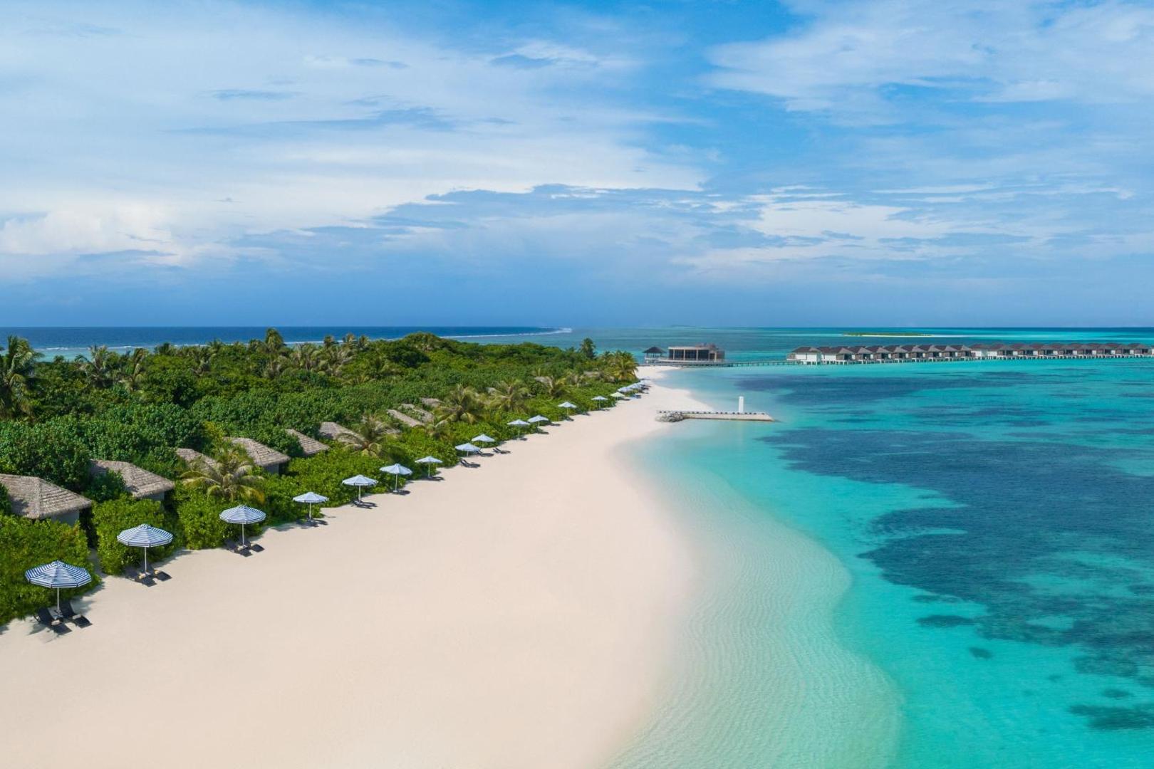 Le Meridien Maldives Resort & Spa aerofoto ar baltu smilšu pludmali, tirkīza lagūnu un ūdens bungalo rindu tālumā