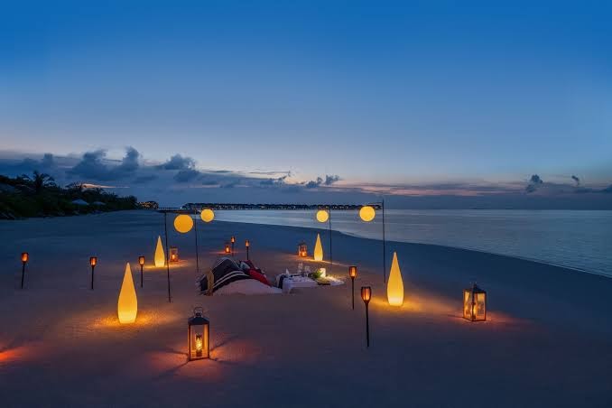 Romantiskas vakariņas pludmalē Le Meridien Maldives Resort & Spa ar laternām, sēžammaisiem un galdu smiltīs krēslas stundā